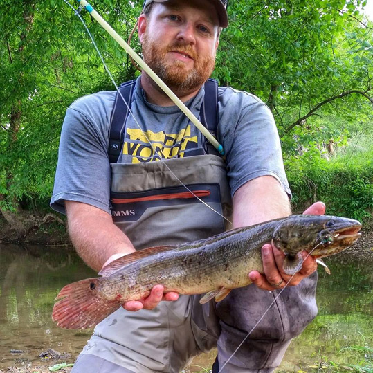 Brandon Bailes holding a bowfin he caught fly fishing in Alabama.
